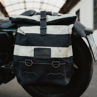 The Holy Freedom Folsom Bag is crafted from 60% cowhide and 40% cotton canvas, this bag combines rugged durability with classic style. The roll-top design offers flexibility and secure storage, while the striped canvas print adds a bold touch. Featuring adjustable leather shoulder straps, a sturdy leather handle with the Holy Freedom writing, and burnished metal hardware. Inside, you'll find a dedicated laptop pocket (fits up to 16 inches) and an internal zip pocket for your essentials. It includes anchors for easy attachment to your bike. With a capacity of 14-18 liters, this 100% handmade bag is ready for any journey. Elevate your adventures with the Holy Freedom Folsom bag!