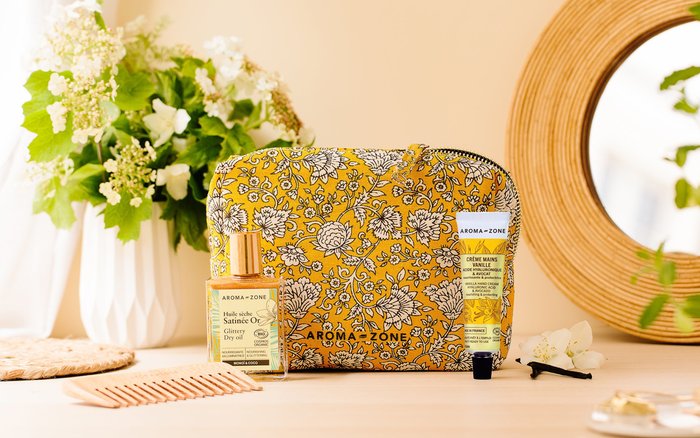 Trousse en tissu fleuri jaune posée près d’une crème pour les mains et d’un flacon d’huile